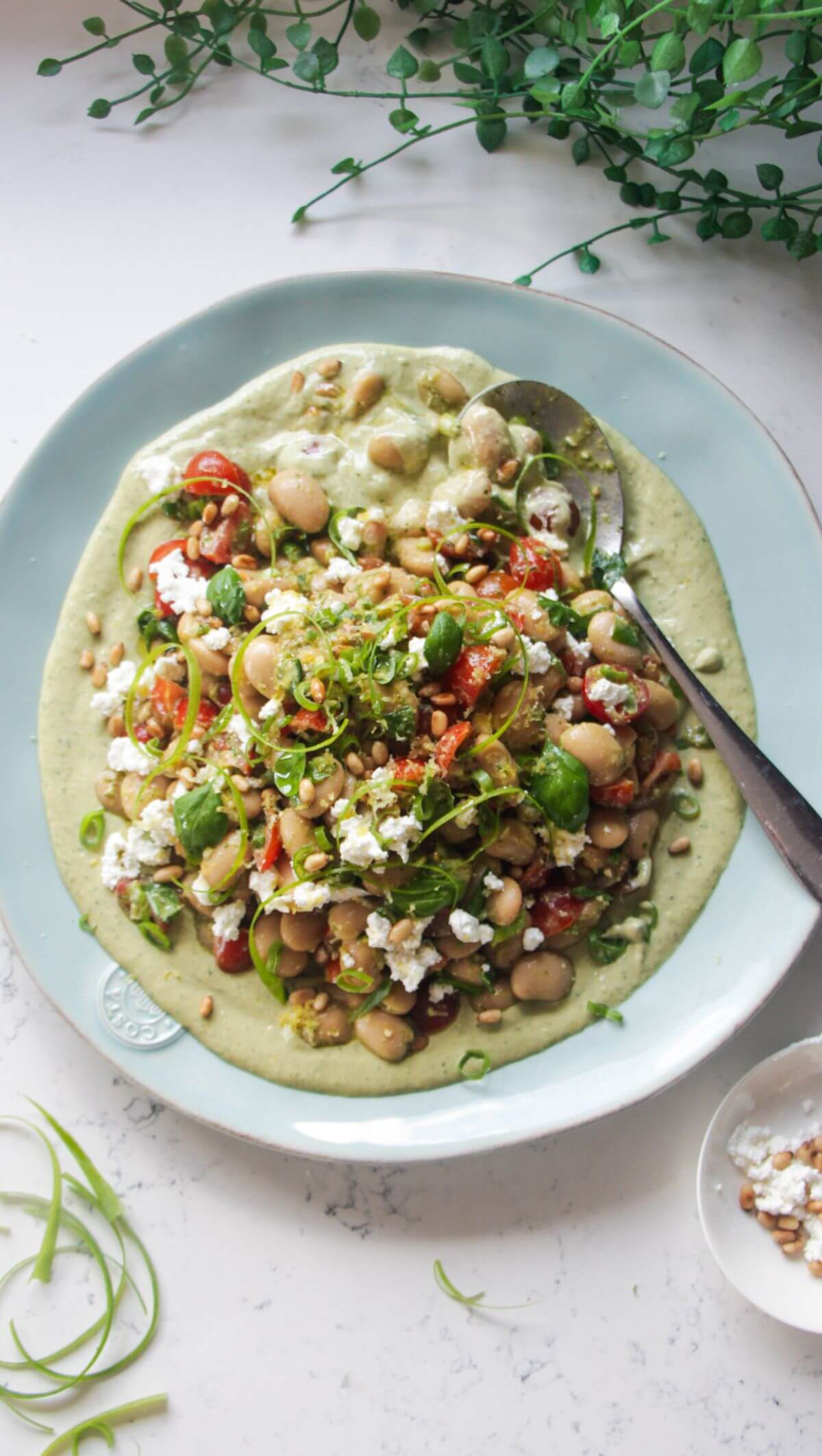 Mediterranean white bean salad on whipped basil tahini on a large light blue serving plate.