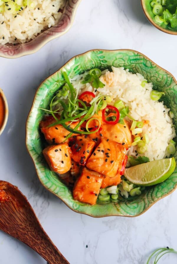 Diced charred salmon on top of rice with scallions and a lime wedge in a small green bowl, with another bowl in the background.
