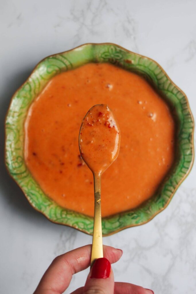 Bright orange bang bang sauce on a spoon, with a bowl of sauce in the background.