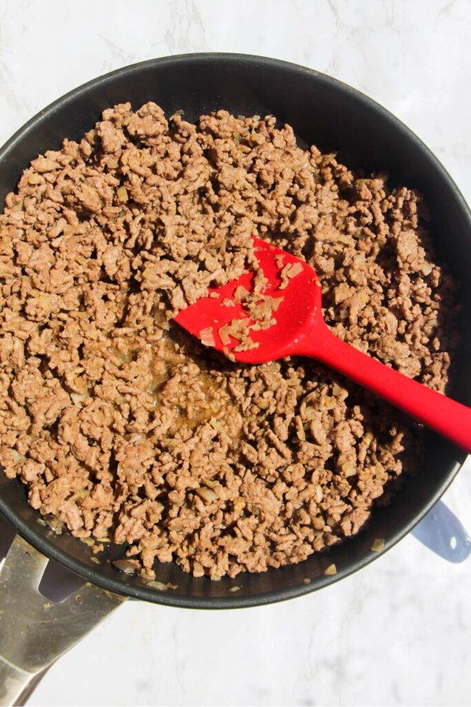 Ground beef browned and cooked in a small pan with a red spatula.