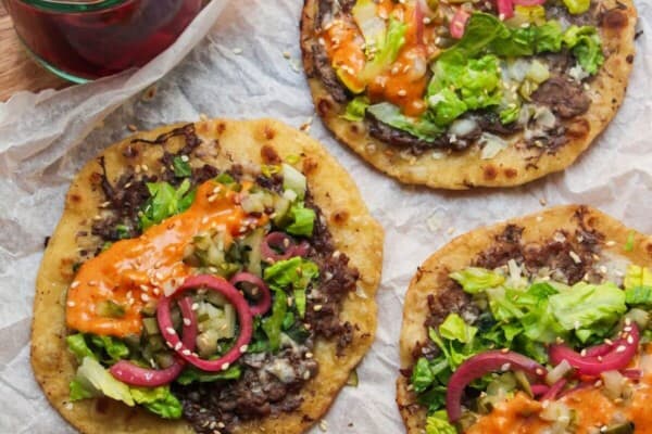 3 Big Mac tacos on a baking paper lined wooden board, with pickles on the side.