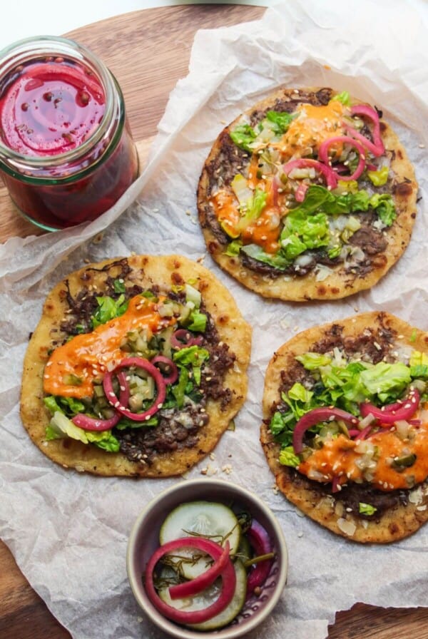 3 Big Mac tacos on a baking paper lined wooden board, with pickles on the side.
