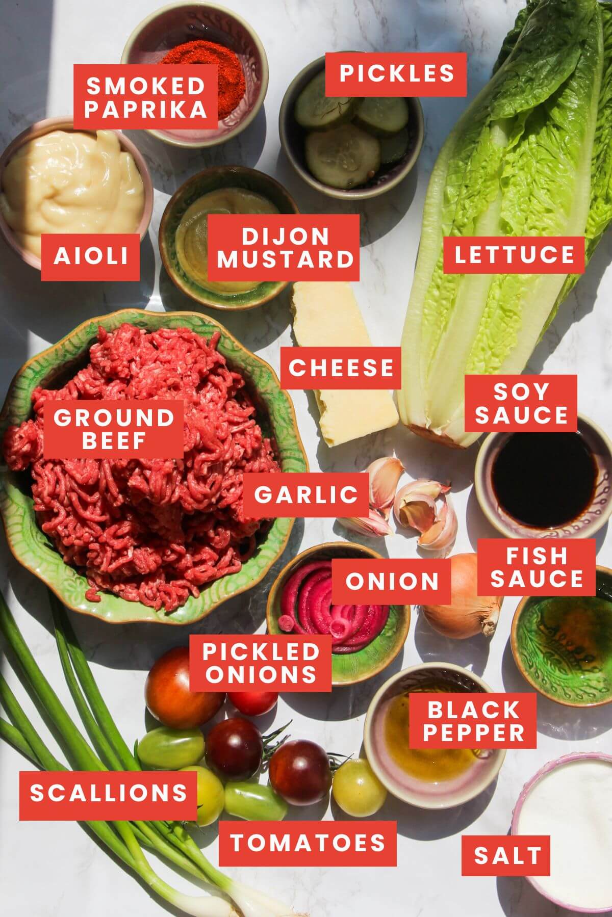 Ingredients for Big Mac salad bowl laid out on a white marble background and labelled.