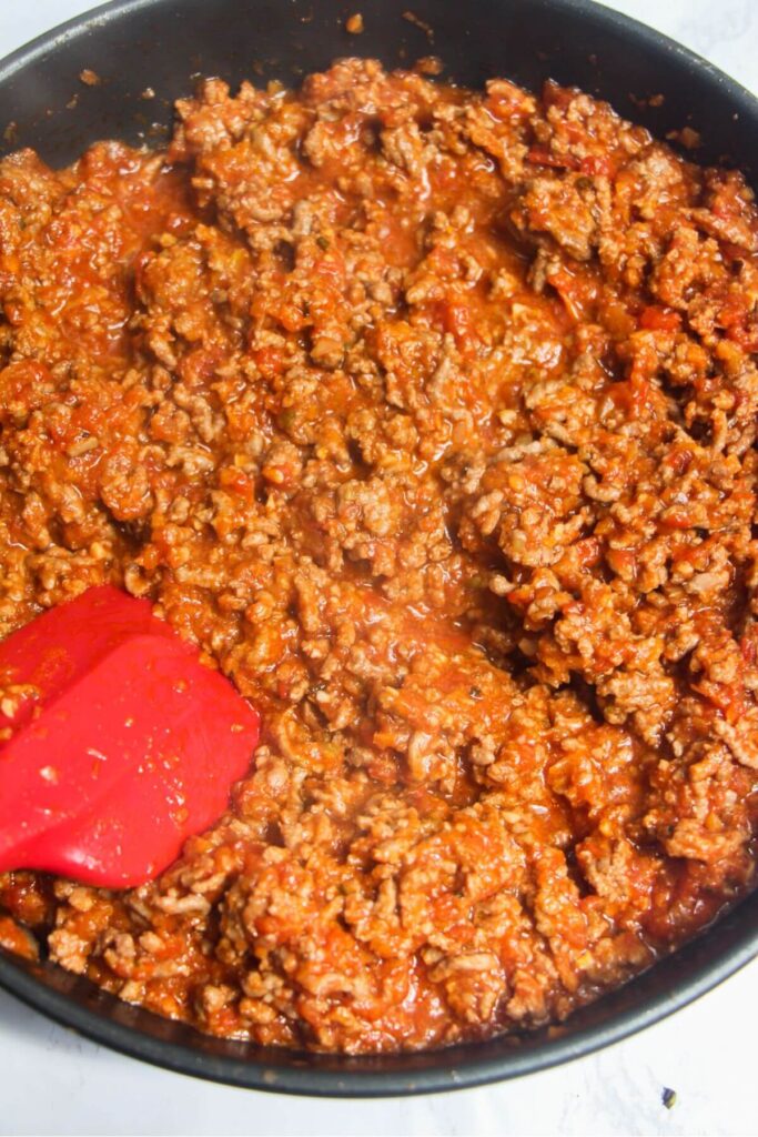 Red spatula stirring cooked bolognese sauce in a pan.