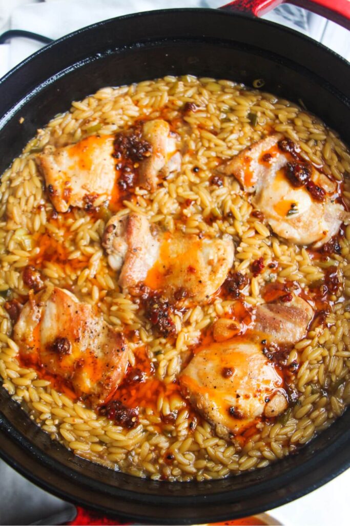 Cooked chicken thighs added into the orzo in a large black pan.