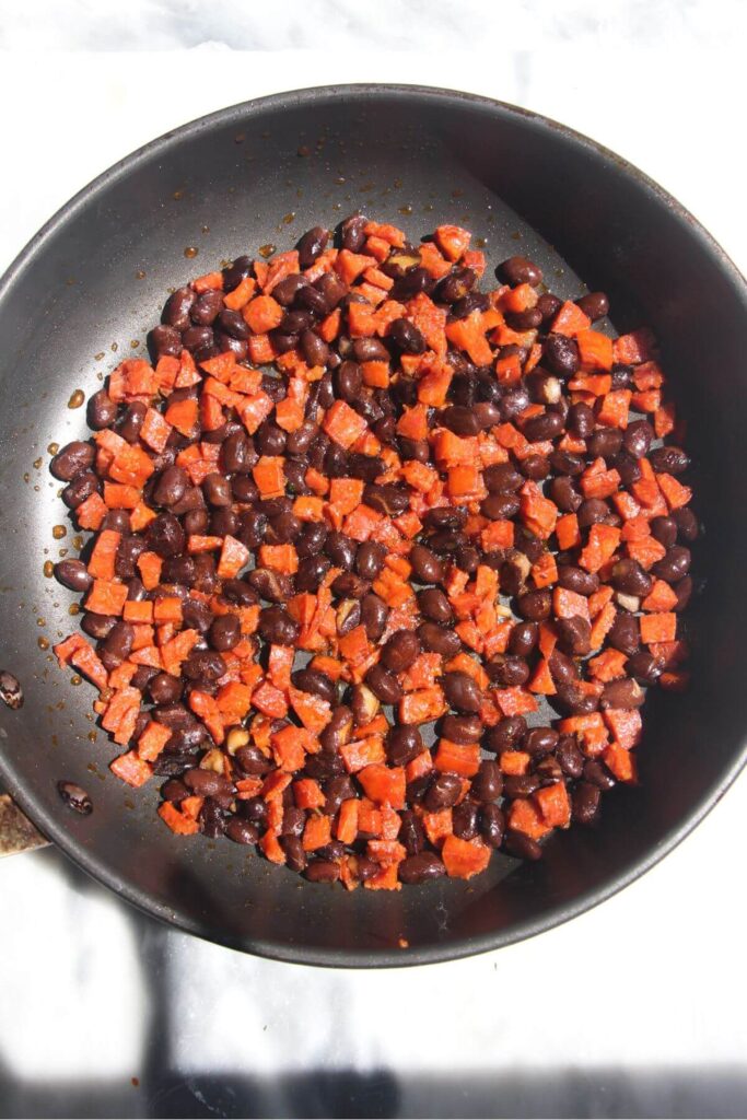 Diced chorizo and black beans in a small black pan.