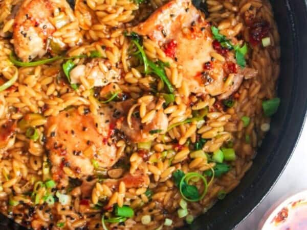 Ginger chicken orzo in a large black skillet, with more chicken orzo in a small plate on the side.