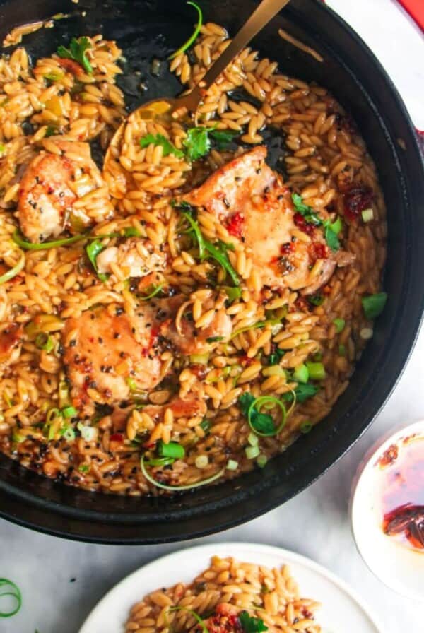 Ginger chicken orzo in a large black skillet, with more chicken orzo in a small plate on the side.