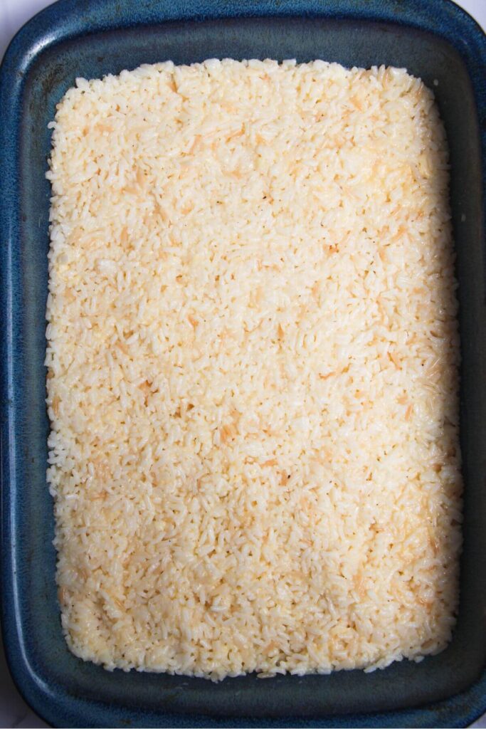 Seasoned rice pressed into a large blue oven dish.