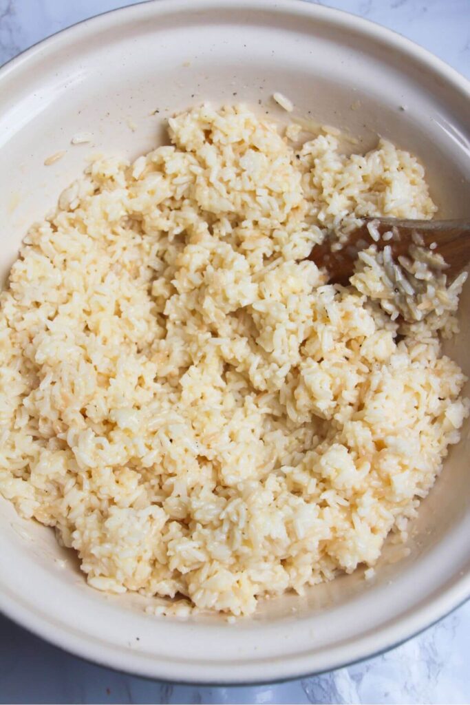 Rice mixed with egg and grated cheese in a large bowl.