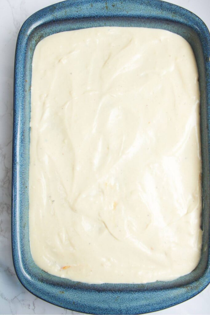 Cheesy bechamel sauce in a large blue oven dish.