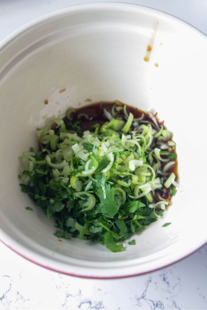 Scallions, cilantro, gochujang paste, soy sauce and chilli jam in a large white bowl.