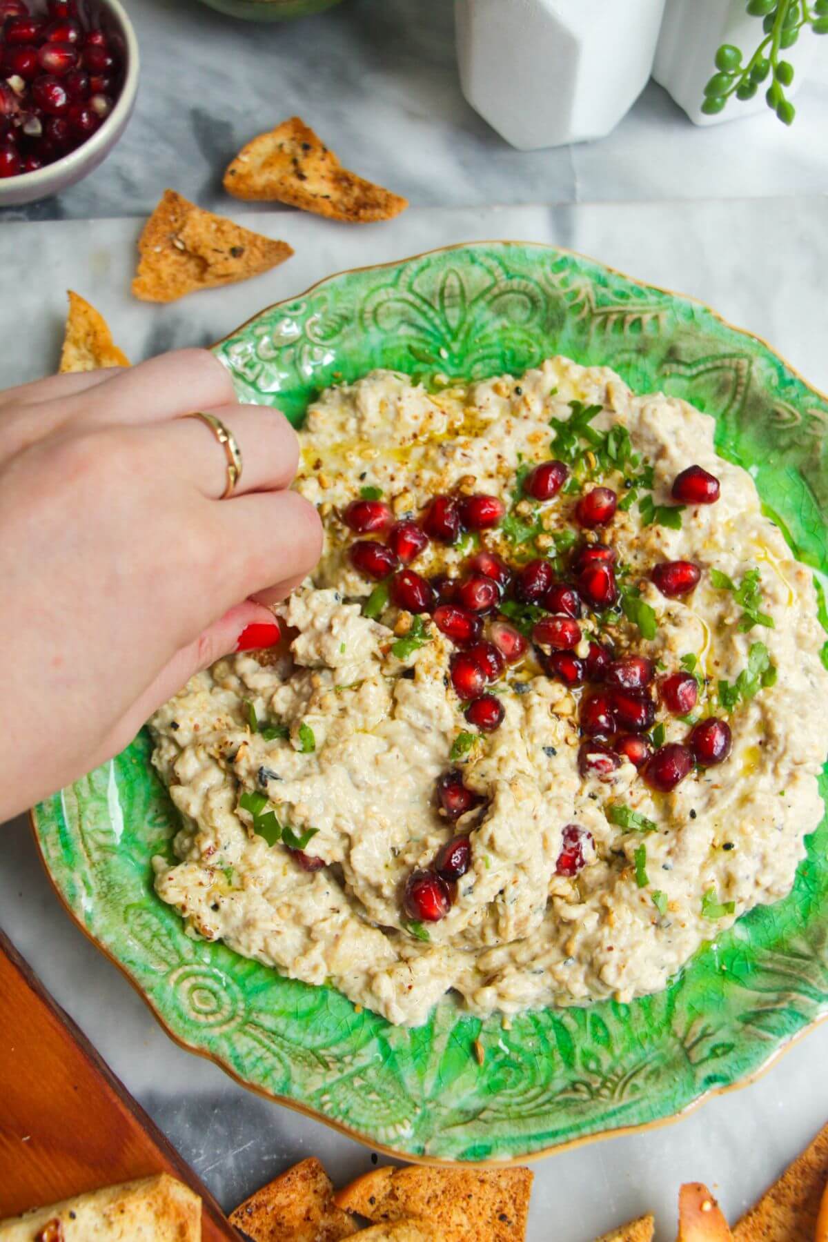 Hand swooping pita chip through smoky eggplant dip on a green plate.