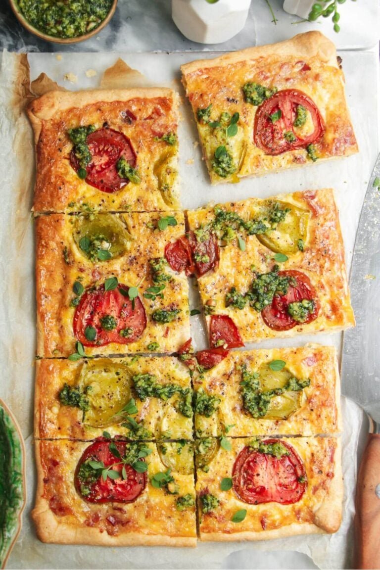 Sliced bacon and egg pie on grey marble background, with pesto and tomatoes on the side.