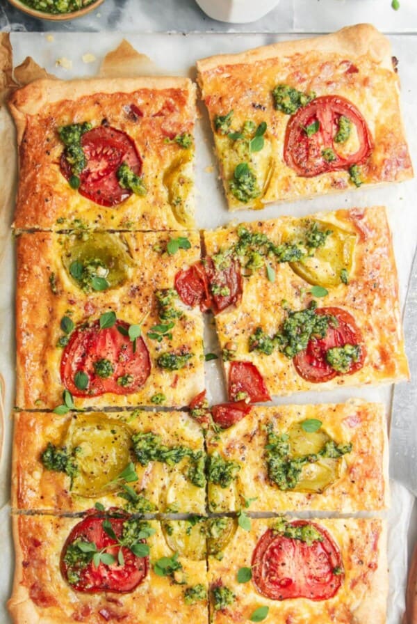 Sliced bacon and egg pie on grey marble background, with pesto and tomatoes on the side.