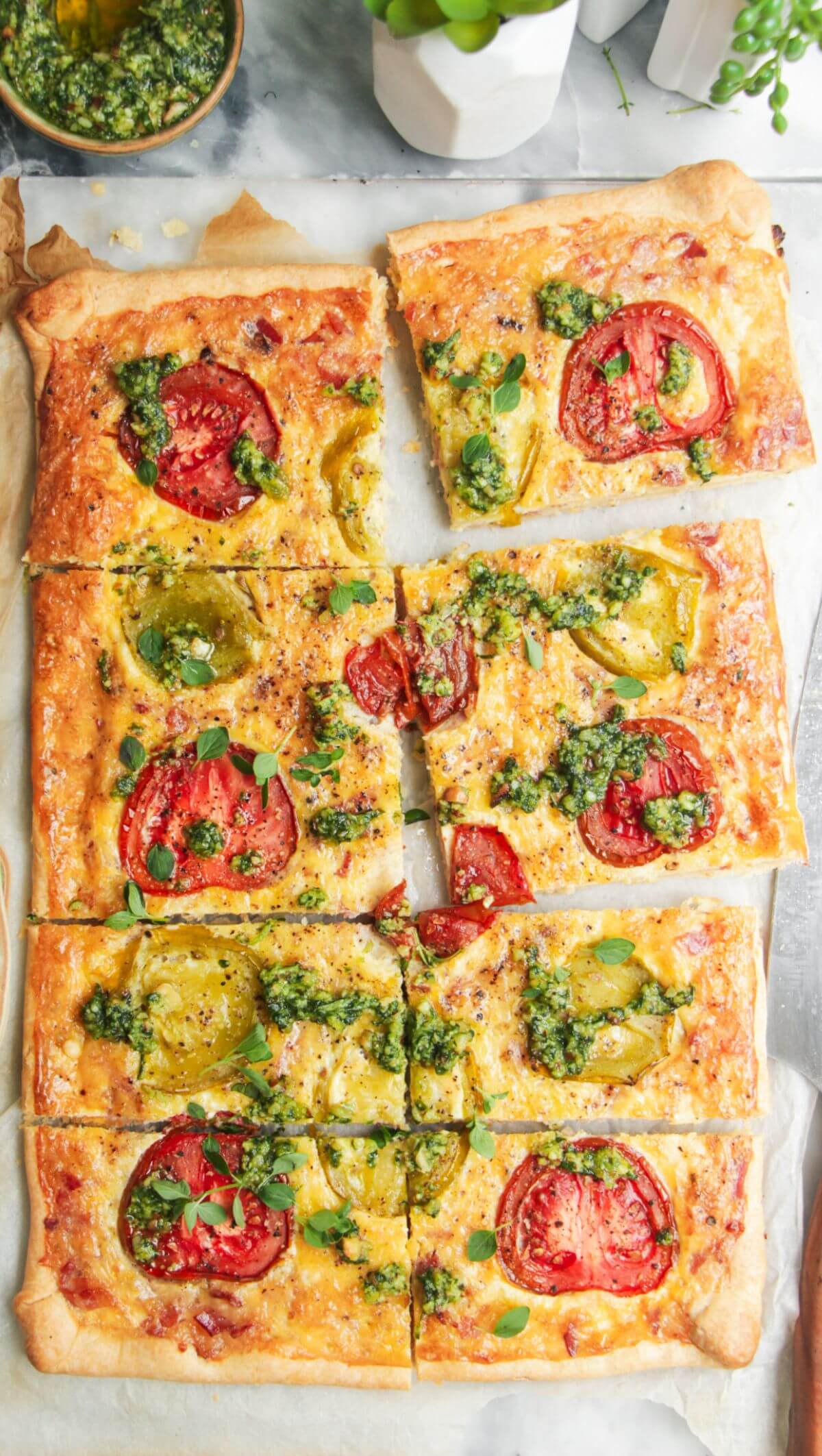 Sliced bacon and egg pie on grey marble background, with pesto and tomatoes on the side.