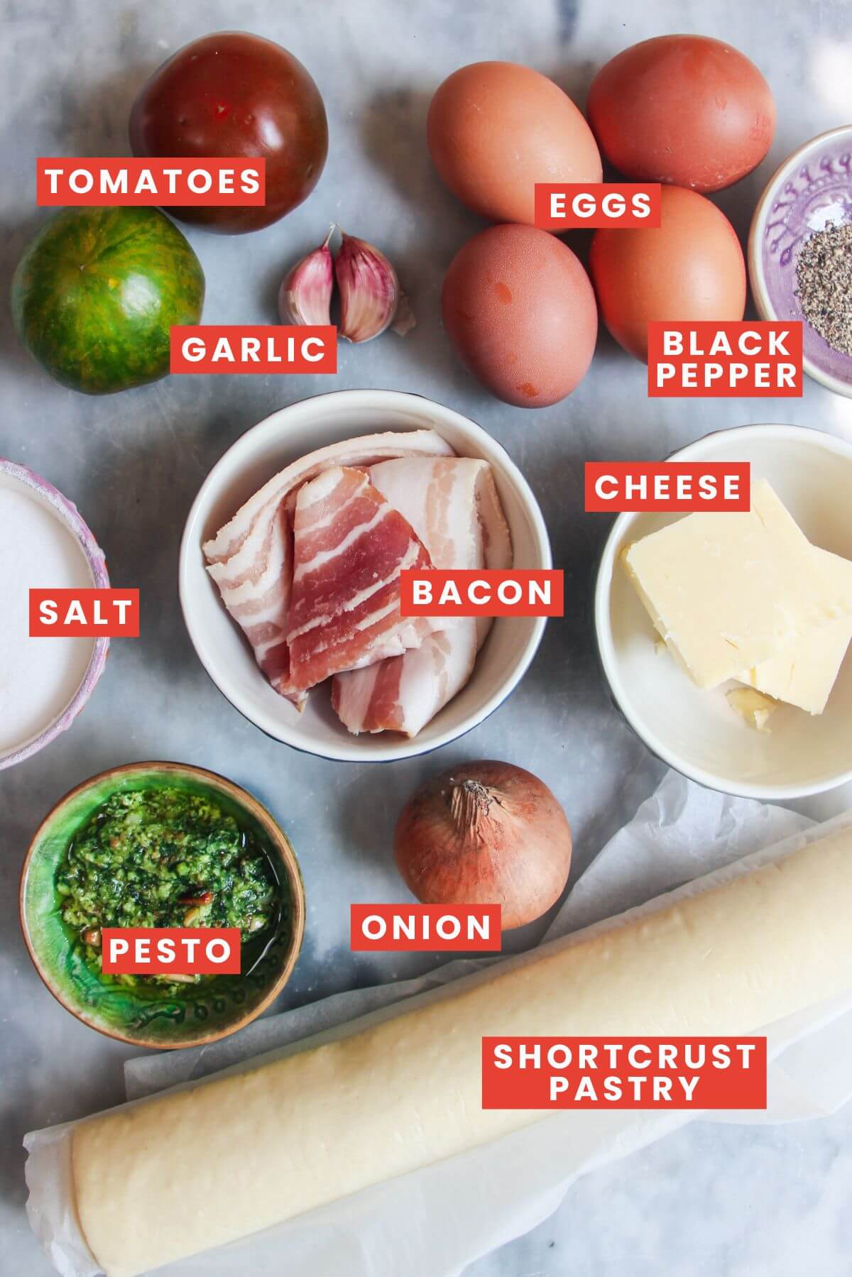 Ingredients for bacon and egg pie laid out on a grey marble background and labelled.