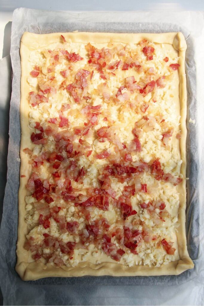 Grated cheese and cooked bacon on top of pastry on a lined oven tray.