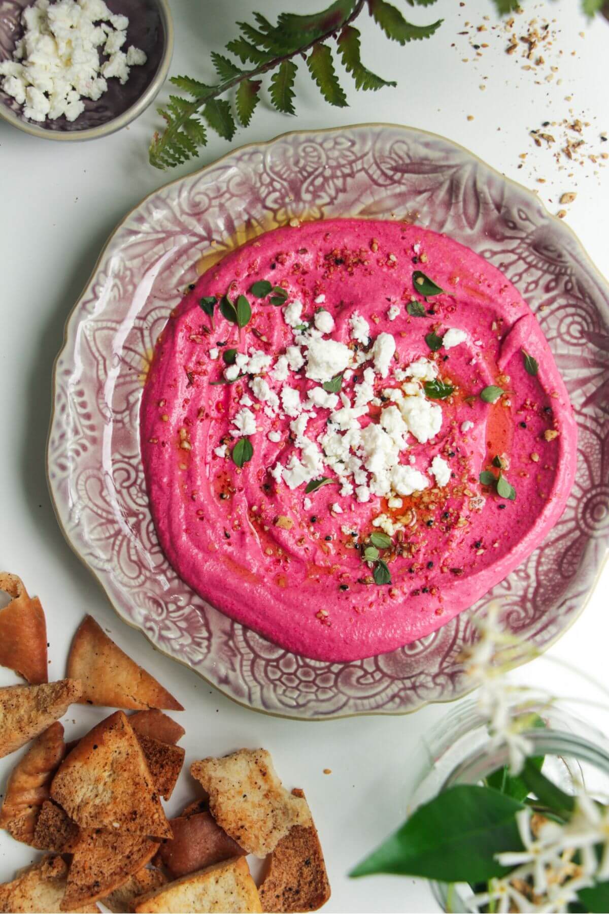 Bright pink beet feta dip on a pink plate with feta crumbled on top and pita chips on the side.