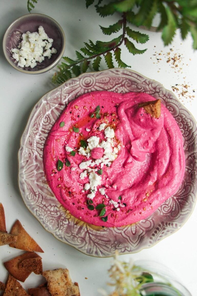 Bright pink beet feta dip on a pink plate with feta crumbled on top and pita chips on the side.