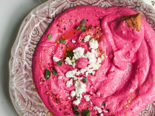 Bright pink beet feta dip on a pink plate with feta crumbled on top and pita chips on the side.