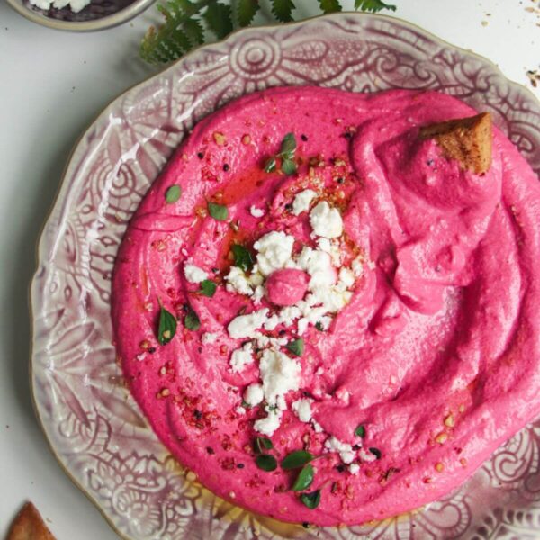 Bright pink beet feta dip on a pink plate with feta crumbled on top and pita chips on the side.
