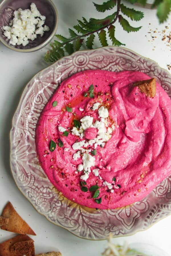 Bright pink beet feta dip on a pink plate with feta crumbled on top and pita chips on the side.