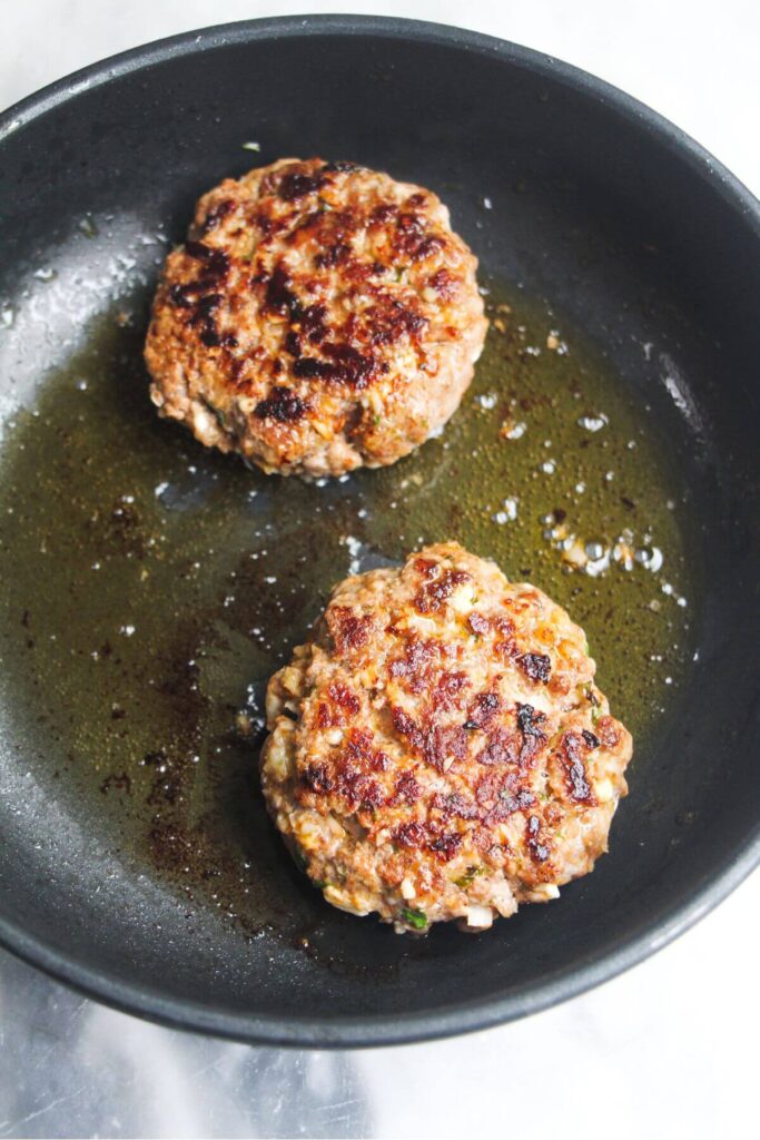 2 lamb burger patties cooked and golden in a small black pan.