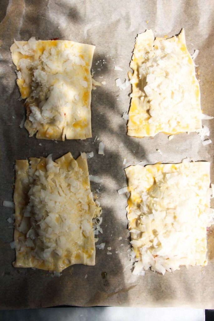 Parmesan topped pastry on top of pizza filling on a lined baking tray.