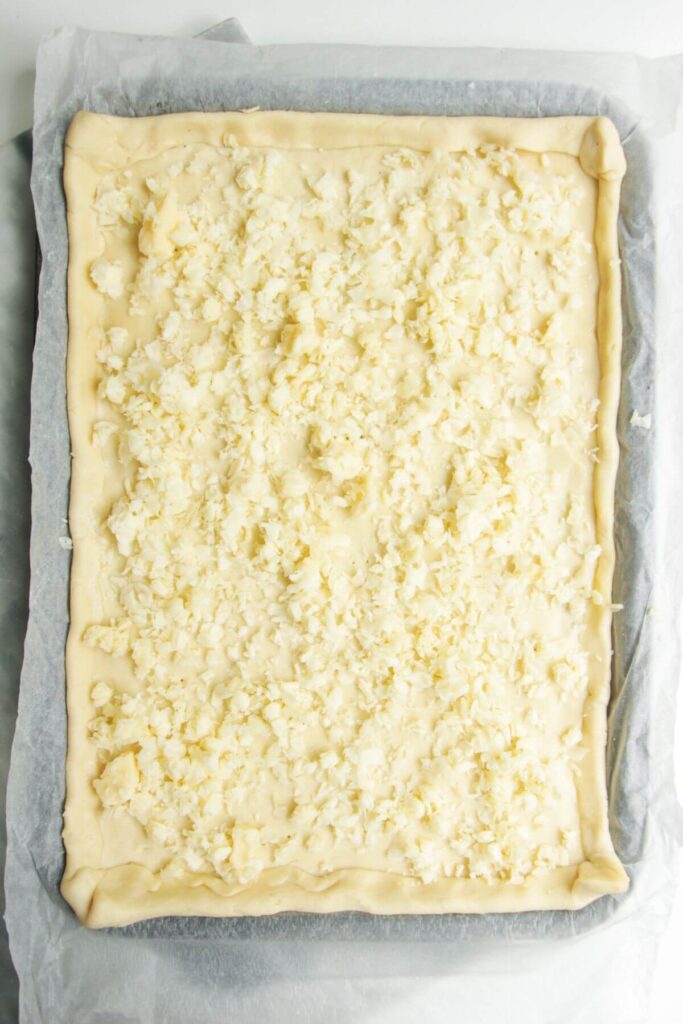 Grated cheese on top of pastry on a baking paper lined oven tray.
