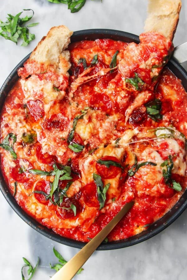 Cheesy pepperoni topped pizza dip with two pieces of bread and a spoon inside.