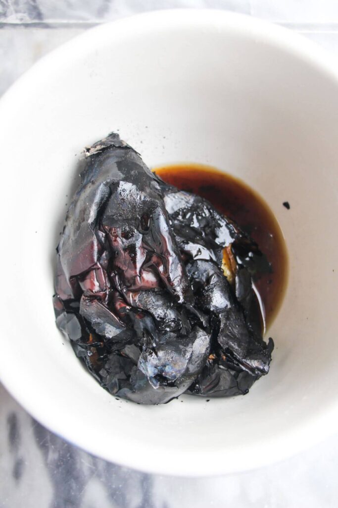 Charred eggplant in a white bowl, with smoky liquid.