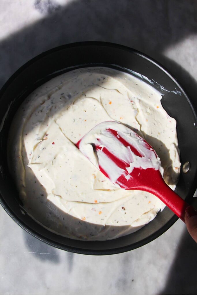 Red spatula smoothing cream cheese mix into small black pan.