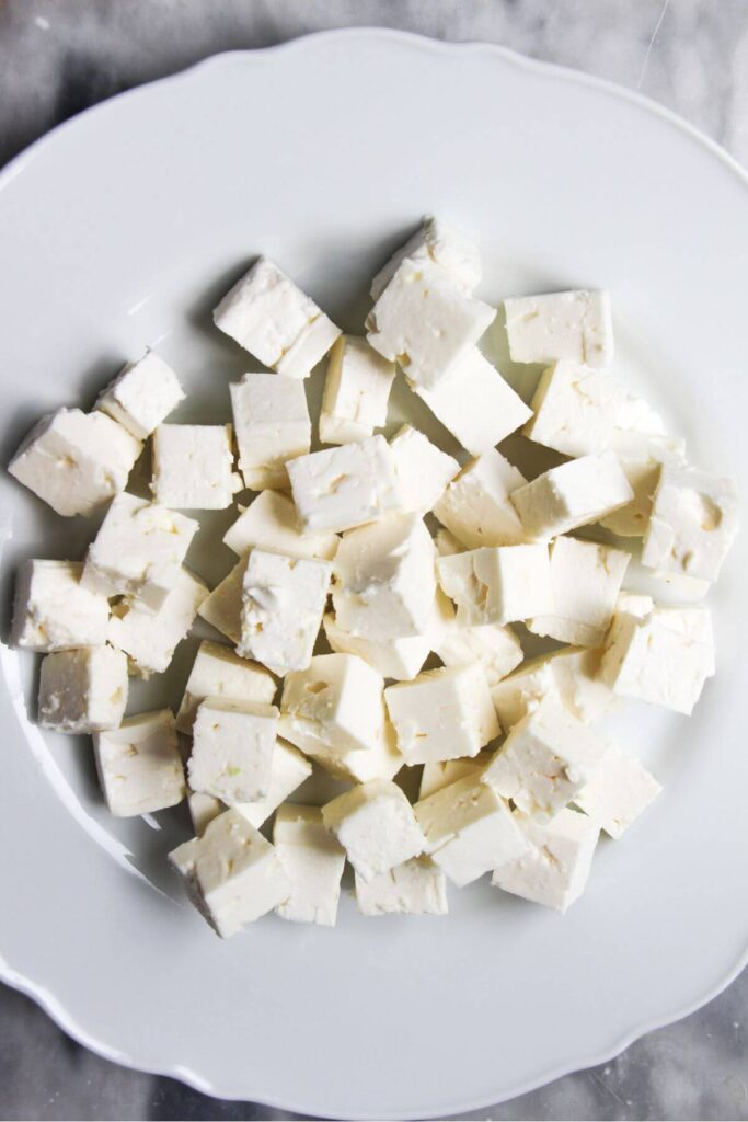 Diced feta on a white scalloped plate.