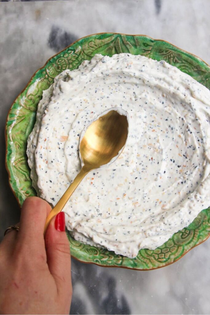 Spooning everything bagel dip onto a small green plate.