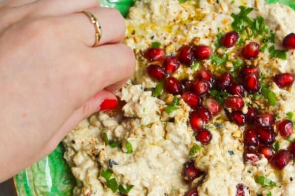 Smoky eggplant dip on a small green plate, with pomegranate seeds on top and pita chips on the side.