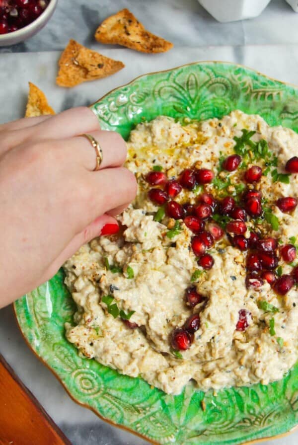 Smoky eggplant dip on a small green plate, with pomegranate seeds on top and pita chips on the side.