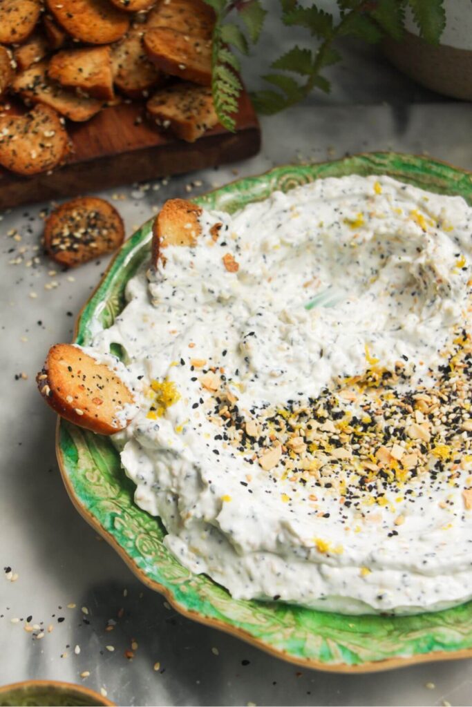 Close up of everything bagel dip with bagel chips on the side on a small green plate.