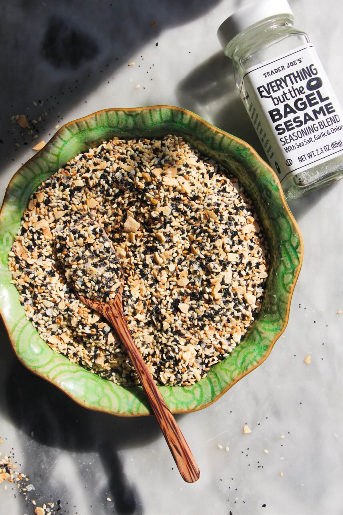Everything bagel seasoning in a green bowl with a wooden spoon inside.