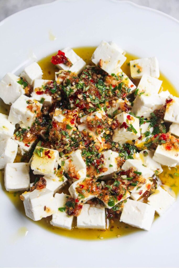 Marinade poured on top of diced feta in a white scalloped plate.