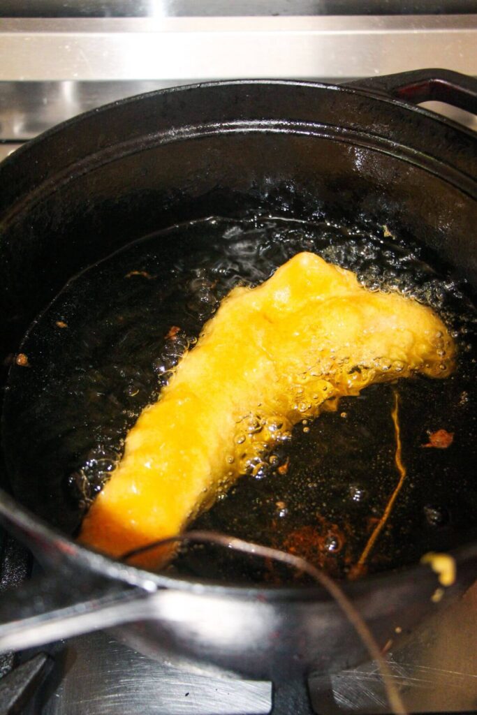 Large battered fish fillet frying in a large pot of oil.