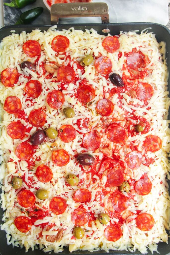 Focaccia pizza topped with cheese, pepperoni and olives in a large oven dish.