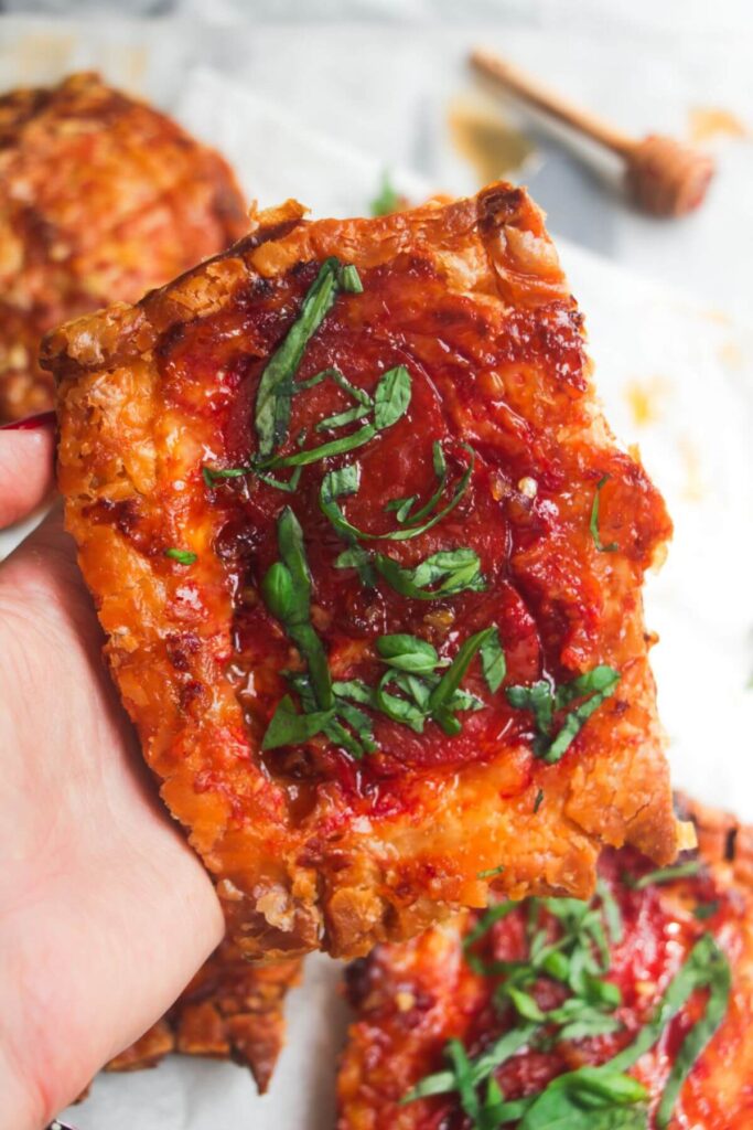 Close up of a hand holding up an upside down puff pastry pizza tart.
