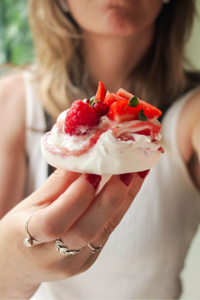 Close up of someone holding up a mini pavlova topped with cheesecake yogurt and mixed berries.