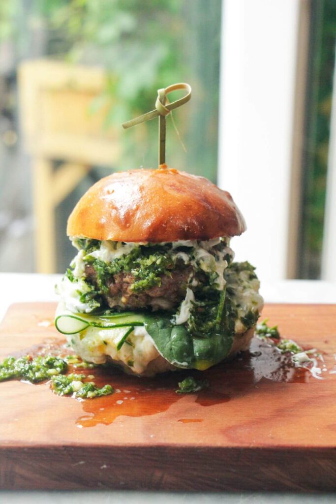 Juicy Greek lamb burger on a small wooden board with a skewer through the top.