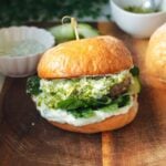 Lamb burger on a wooden board, with tzatziki and spinach.