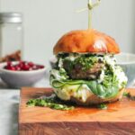Juicy Greek lamb burger on a small wooden board with a skewer through the top.