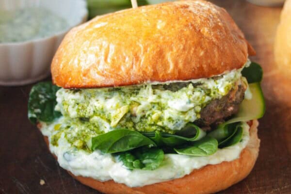 Lamb burger on a wooden board, with tzatziki and spinach.