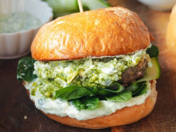 Lamb burger on a wooden board, with tzatziki and spinach.