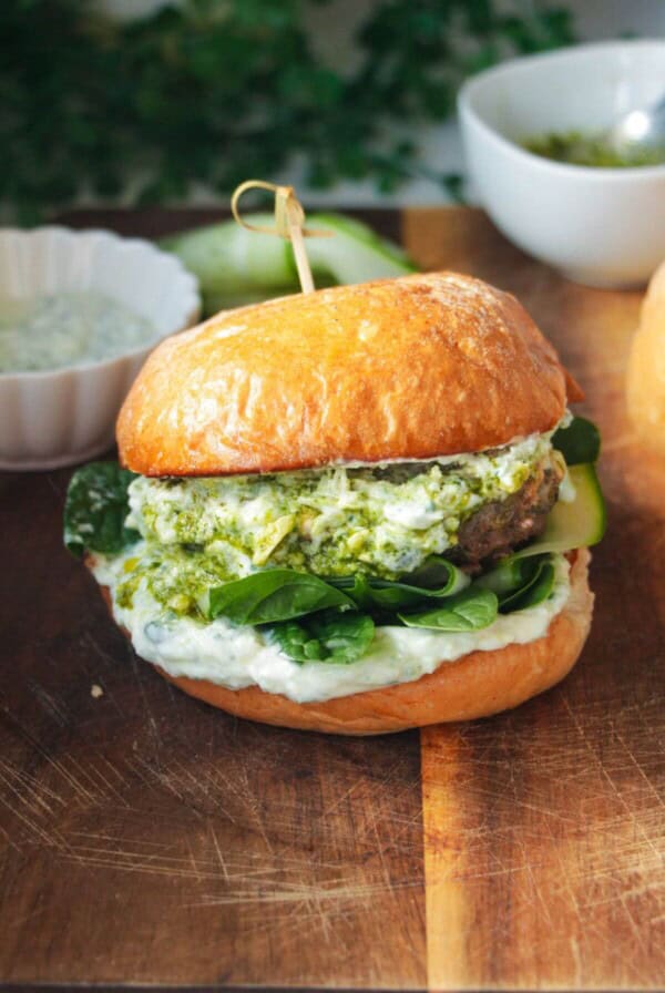 Lamb burger on a wooden board, with tzatziki and spinach.